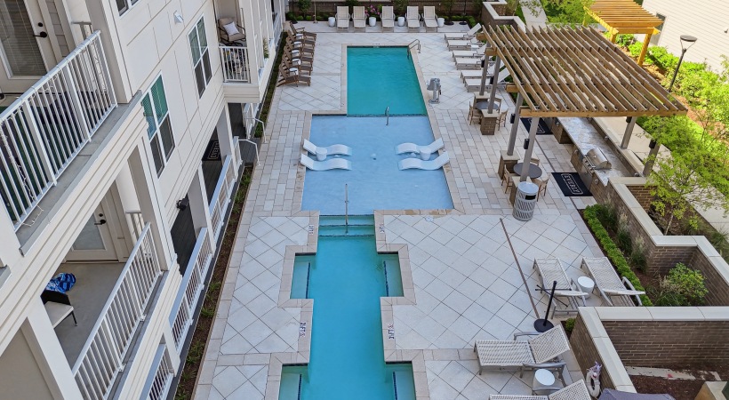  A large swimming pool surrounded by an apartment building and a patio.
